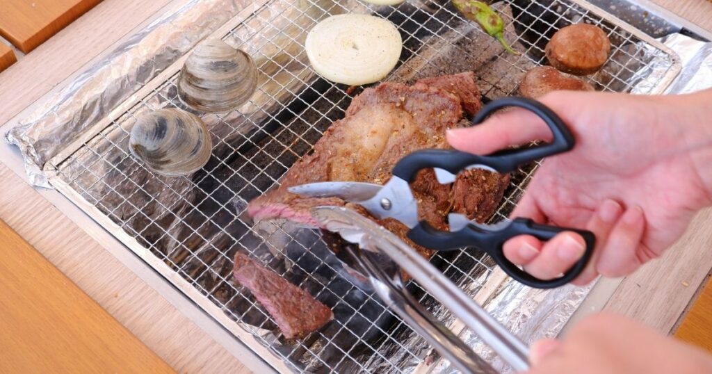 網の上で焼いているステーキ用牛肉肩ロースを切る